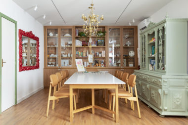 na foto mesa com seis cadeiras, duas estantes de madeira, lustre de ferro e espelho com moldura vermelha