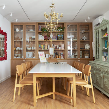 na foto mesa com seis cadeiras, duas estantes de madeira, lustre de ferro e espelho com moldura vermelha