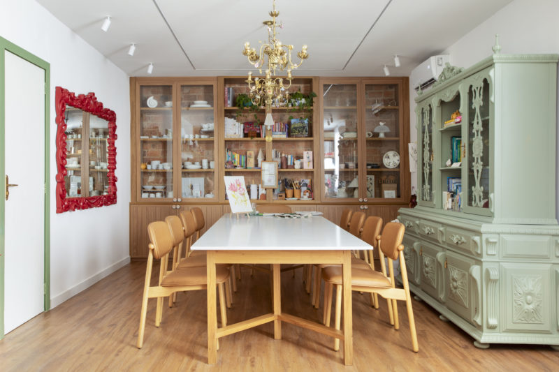 na foto mesa com seis cadeiras, duas estantes de madeira, lustre de ferro e espelho com moldura vermelha