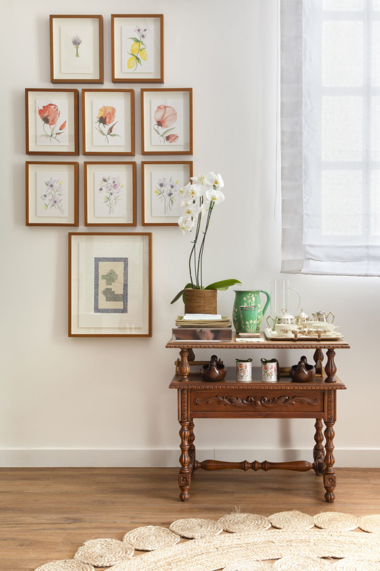 na foto uma mesinha de madeira e quadros na parede branca