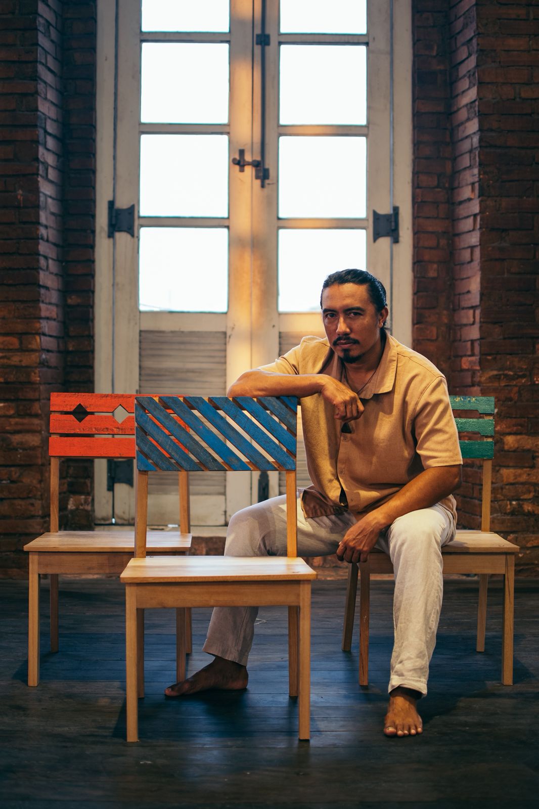 na foto um homem sentado em uma cadeira e uma grande janela atrás