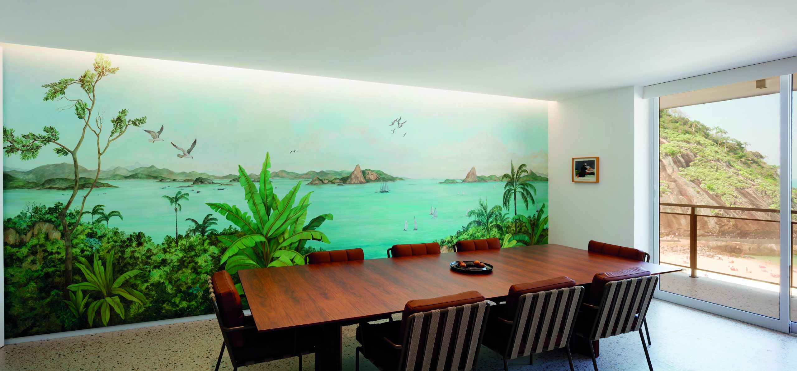 na foto uma sala com mesa de jantar de madeira e um imenso quadro de paisagem atrás