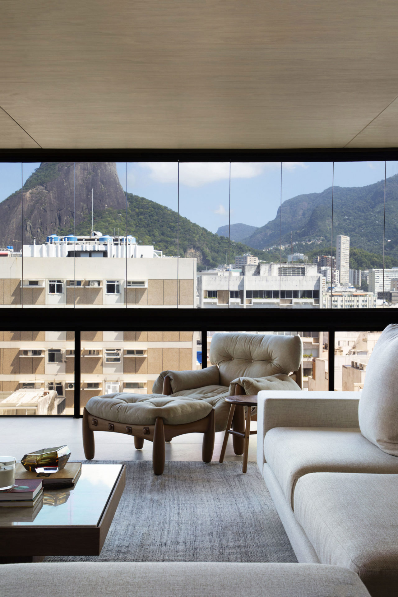 na foto sala de apartamento com grande janela e poltrona mole de couro