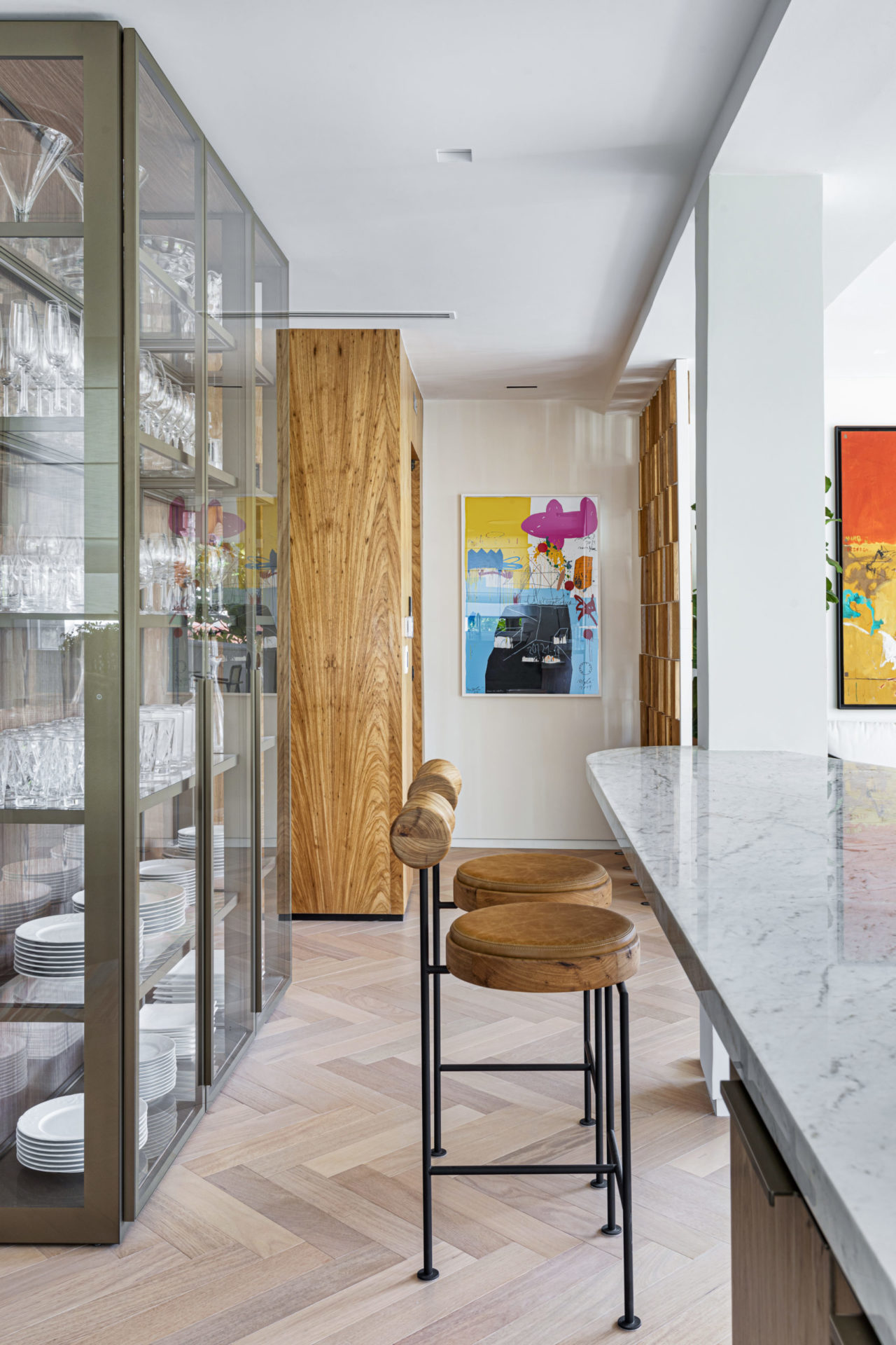 na foto uma cristaleira, uma bancada com banquetas e um quadro na parede