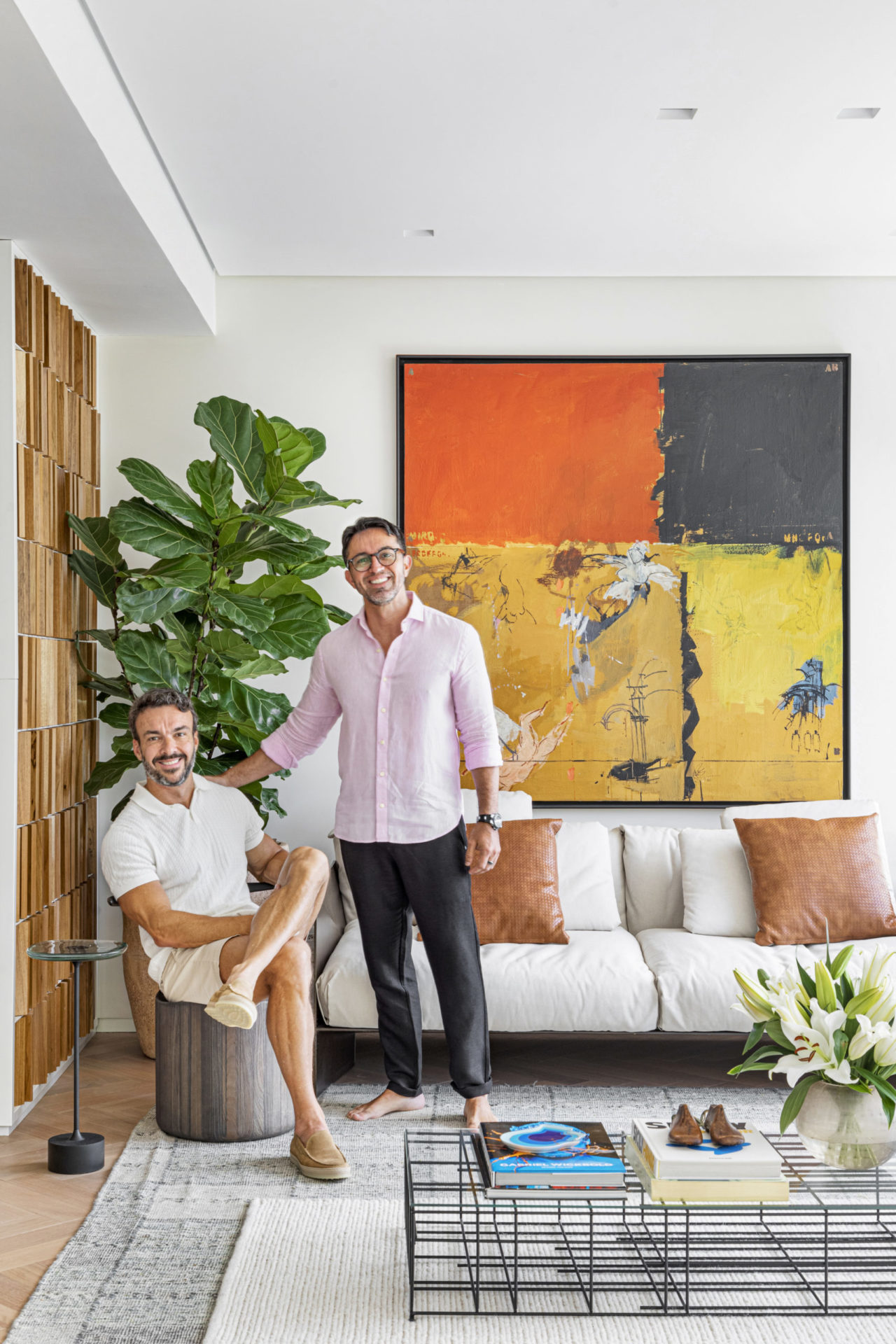 na foto dois homens brancos, um de pé e outro sentado, em uma sala