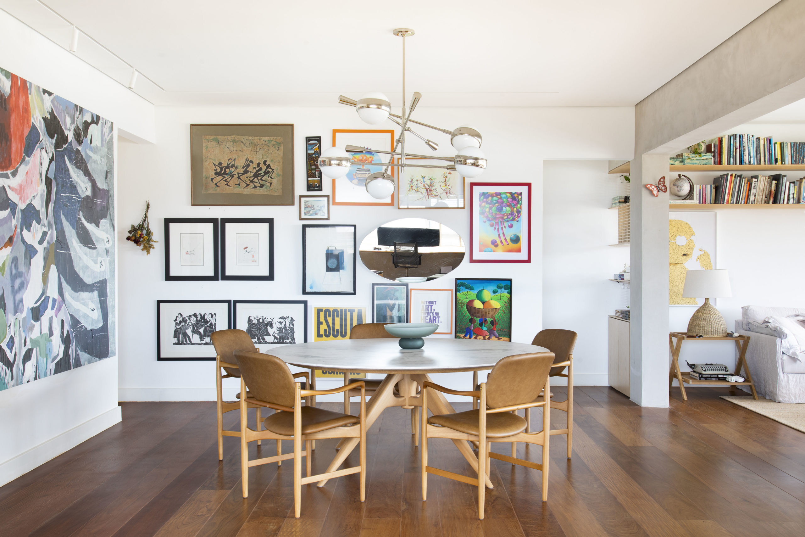 na foto sala de jantar com mesa redonda, paredes brancas e com quadros