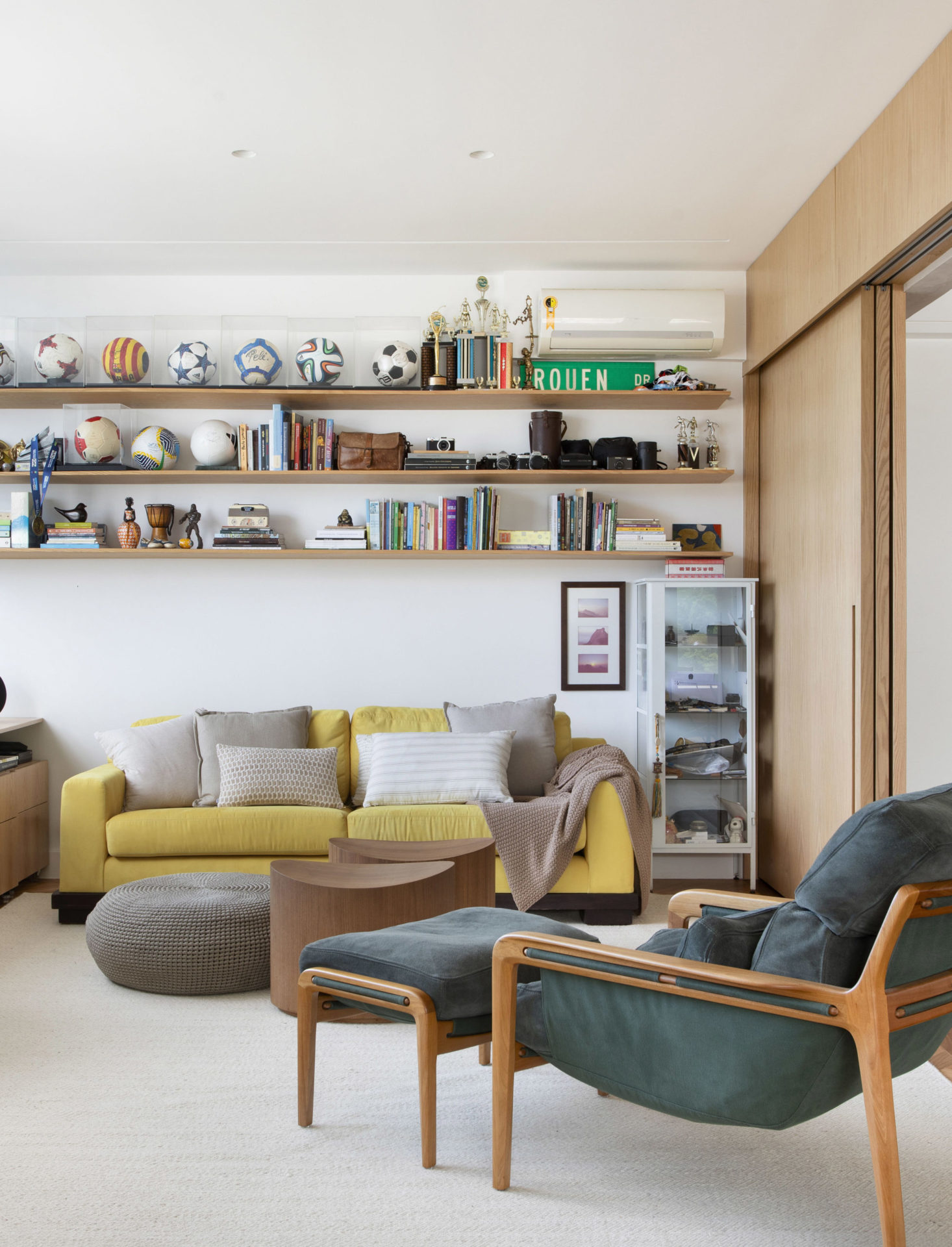 na foto cômodo com sofá mostarda, prateleiras e poltrona verde