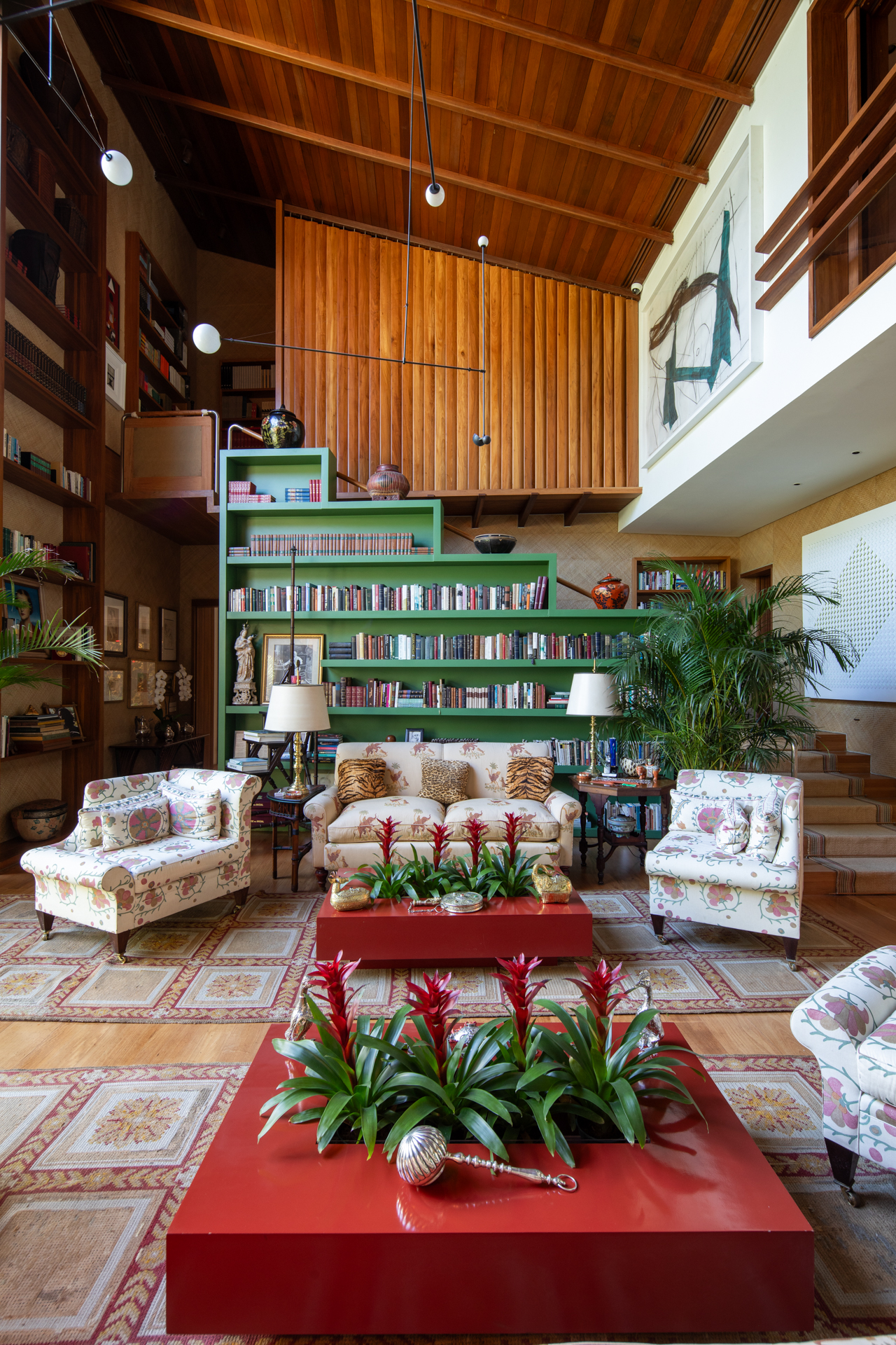 Sala com muita luz natural, uma enorme estante verde abrigada a biblioteca, pé direito muito generoso.