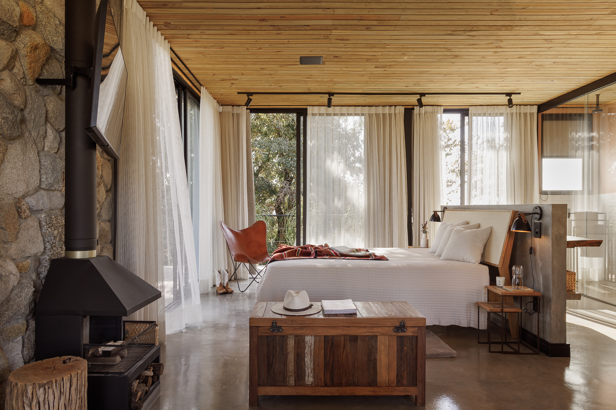 na foto quarto de casal de cabana metálica com grandes janelas e cortinas