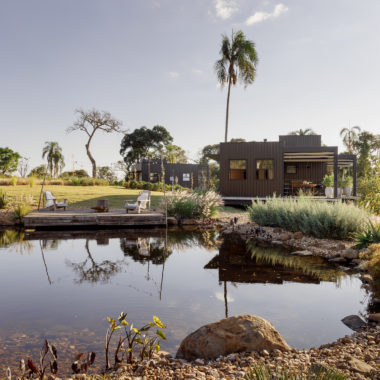 na foto área externa da cabana metálica com grande lago em seu entorno