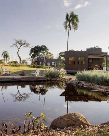 na foto área externa da cabana metálica com grande lago em seu entorno