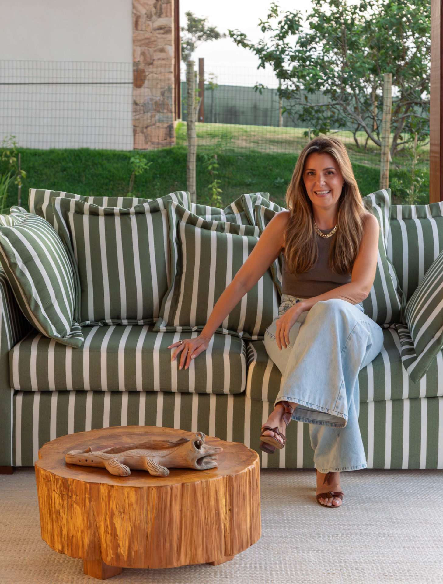 na foto mulher loira sentada em um sofá branco e verde em varanda gourmet de casa de praia