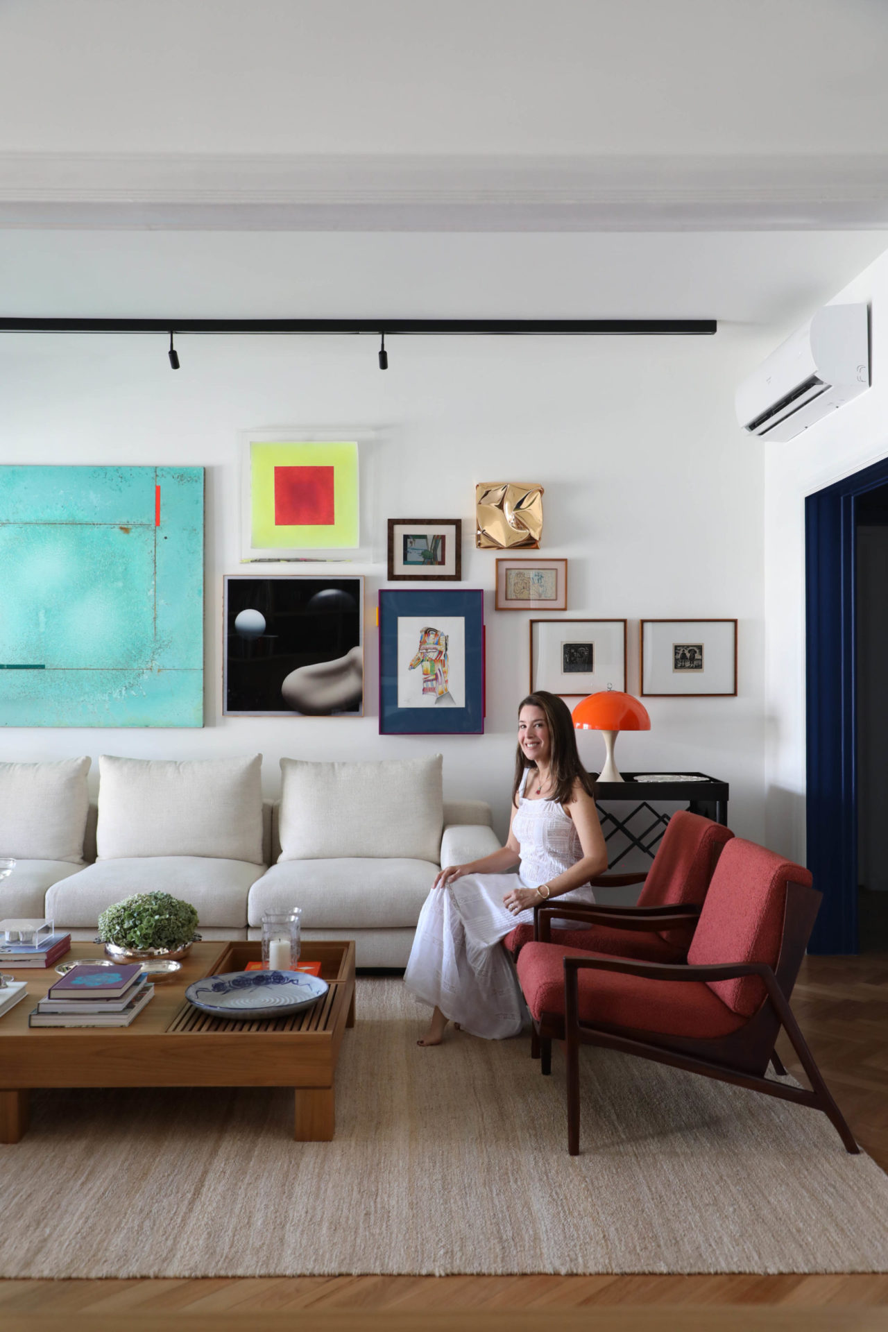 na foto sala de estar com mulher branca de cabelos castanhos sentada em uma poltrona