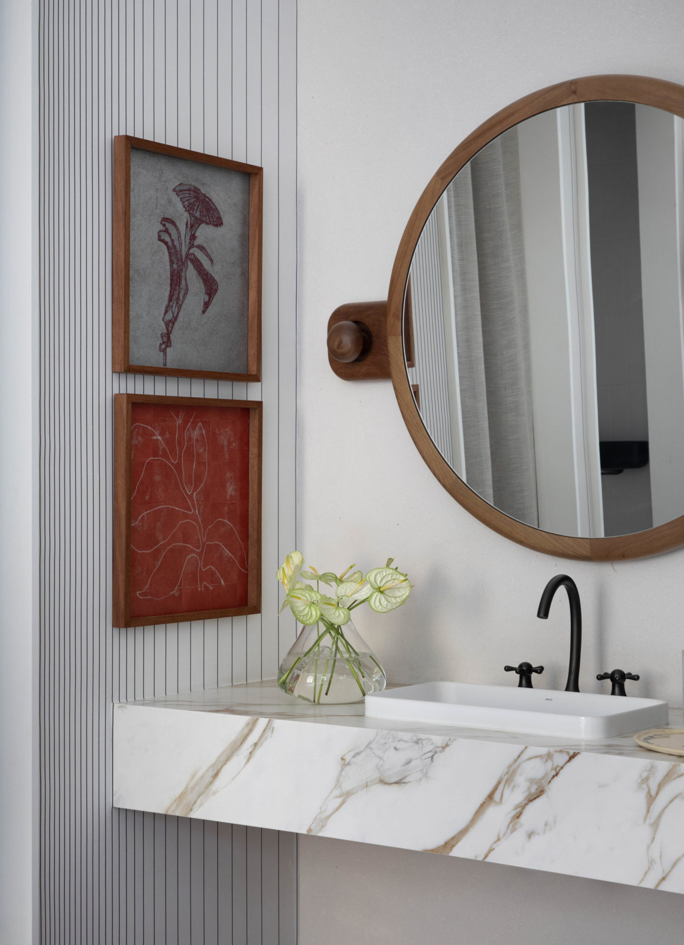 na foto banheiro com espelho redondo, quadros na cor camim e pia em mármore
