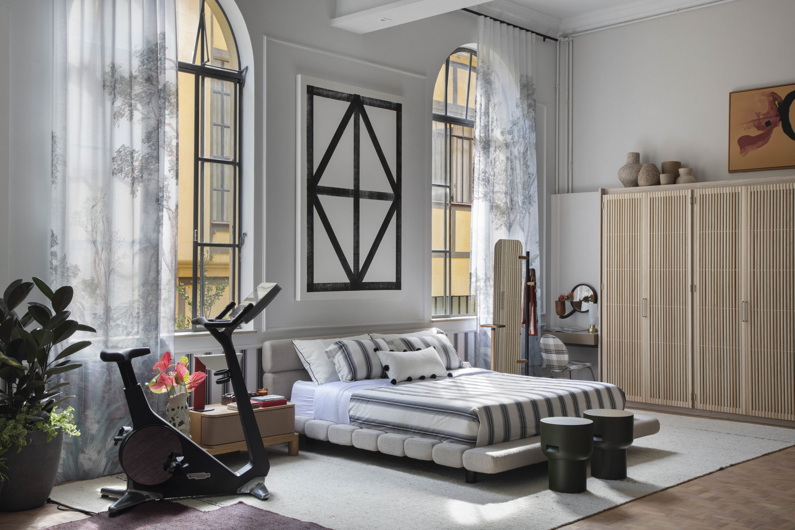 na foto quarto de loft com cama, grandes janelas, bicicleta e armário