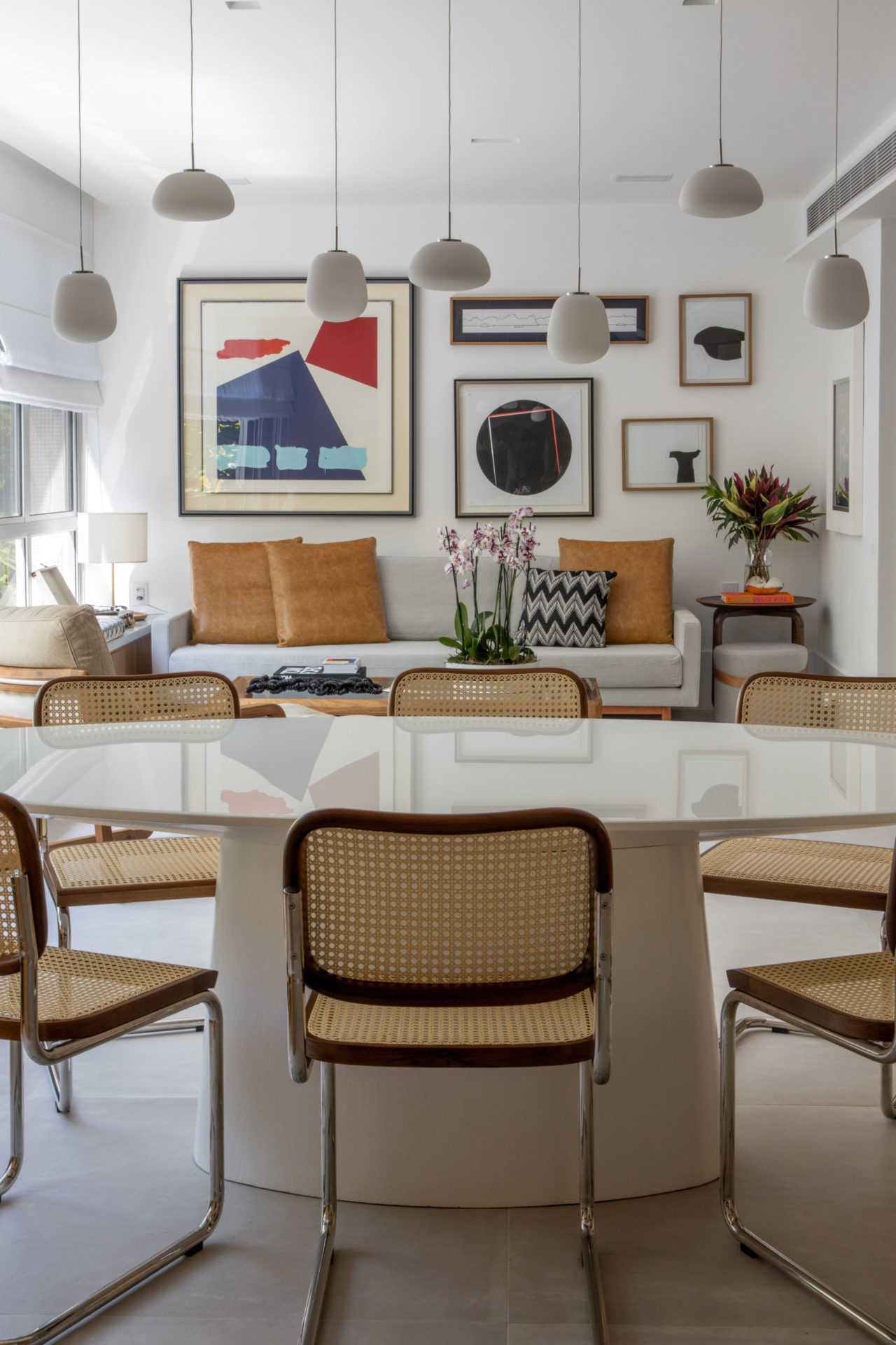 na foto sala de estar de apartamento. na parede muitos quadros coloridos. sofá branco e mesa de jantar