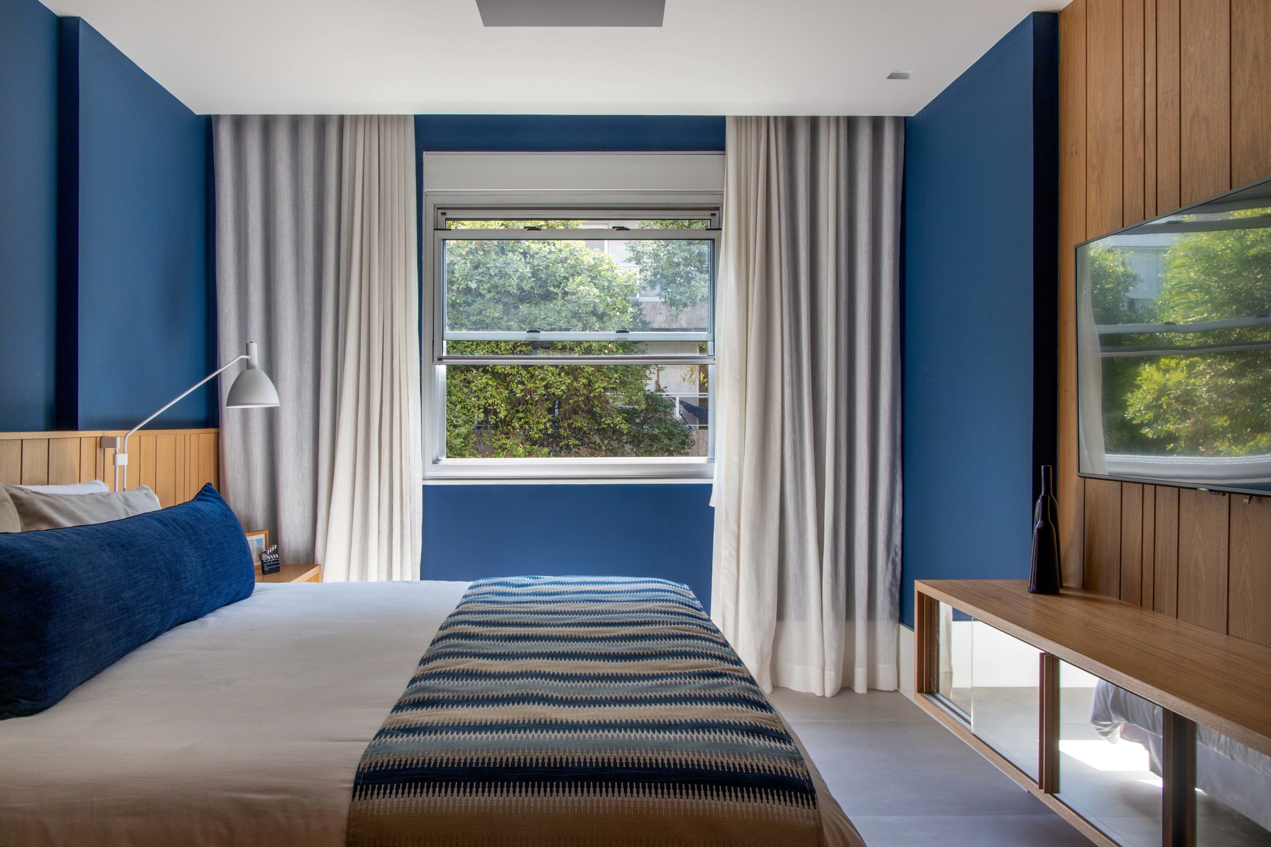 na foto quarto com cama de casal, janela com cortina branca e paredes azuis