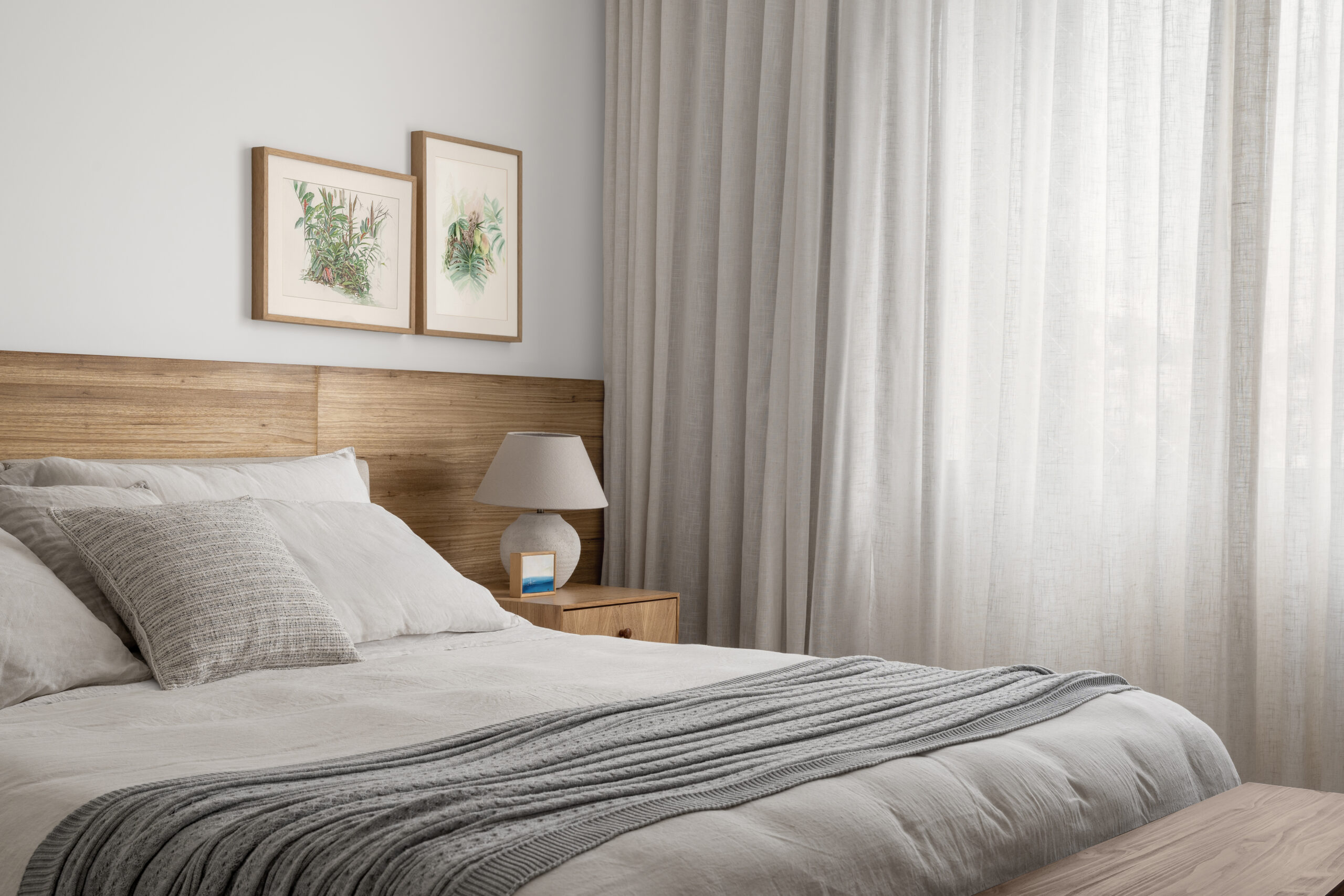 na foto quarto com cama de casal, janela, cortina branca e quadros na parede