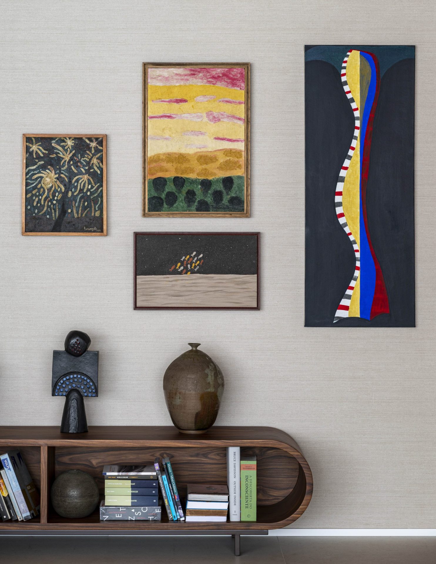 na foto cômodo de apartamento com quadros na parede e obras de arte em um aparador. Parede branca. 