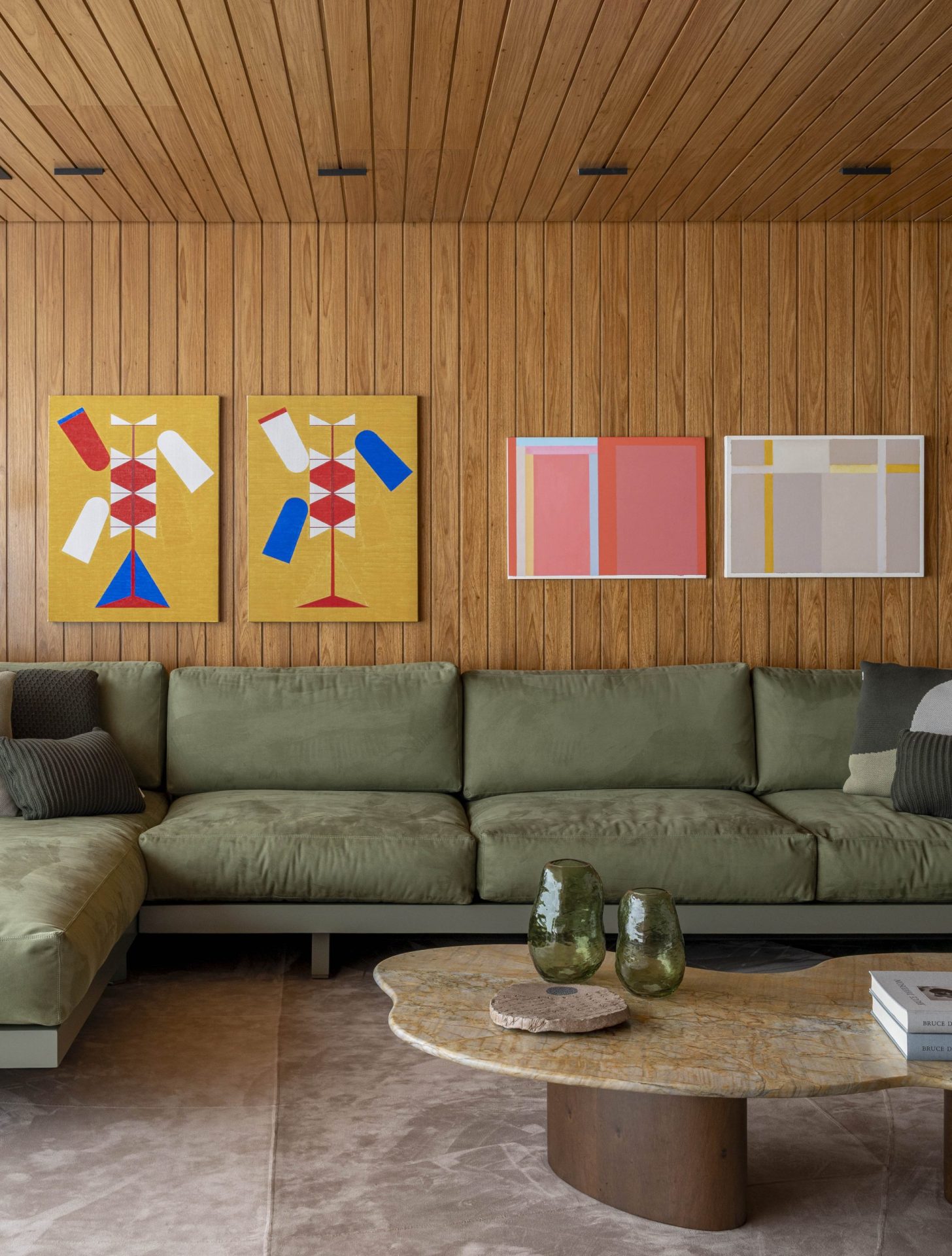 na foto sala com parede em madeira, quadros pendurados e um sofá em L verde