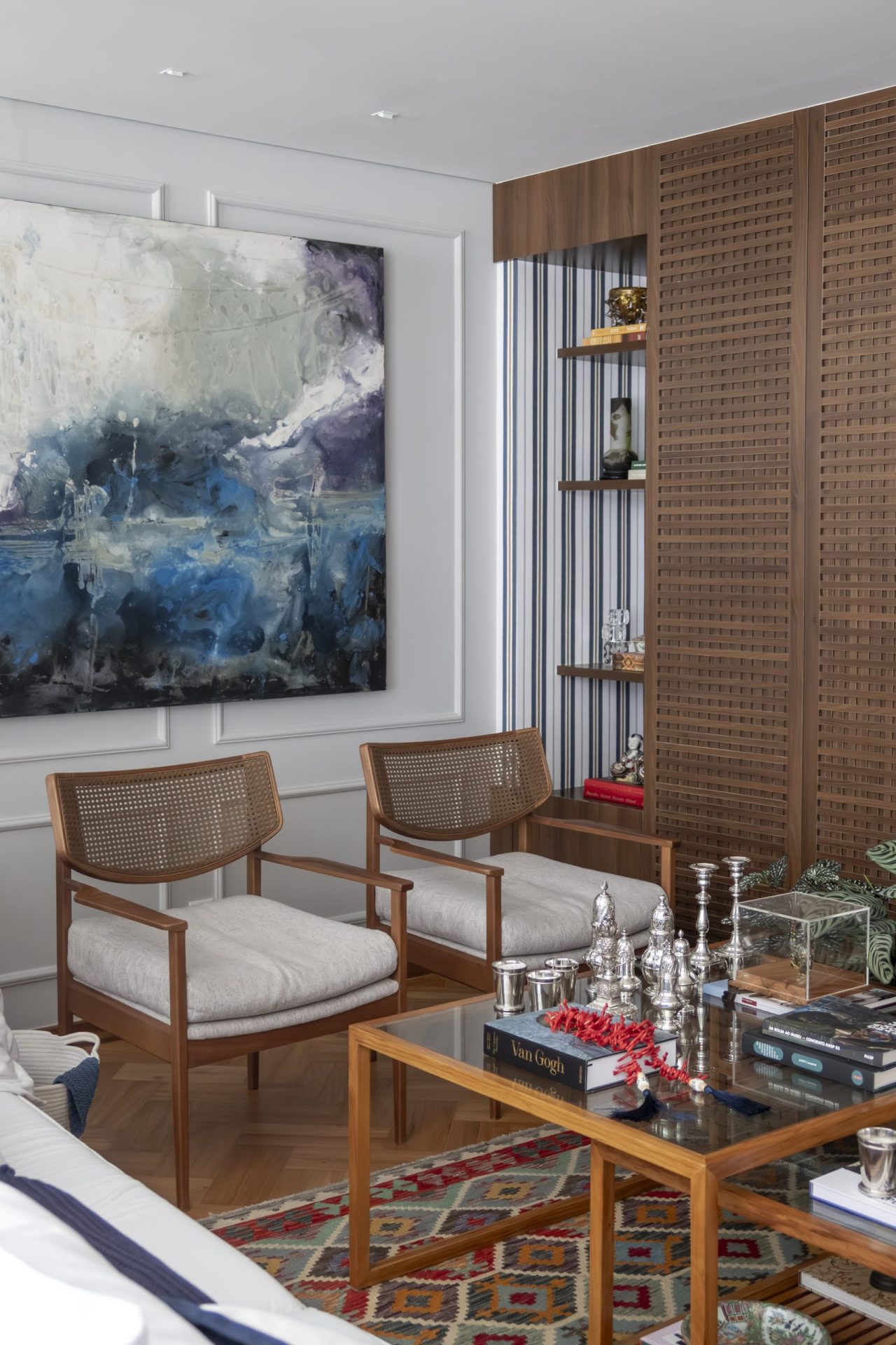 na foto duas poltronas, um quadro quadrado na parede e parte de uma estante de madeira com objetos de decoração
