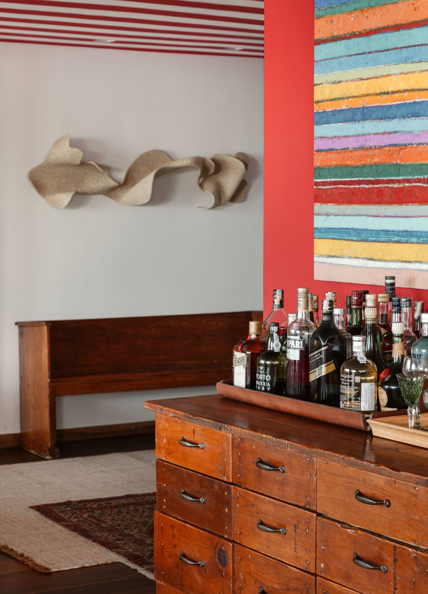 na foto cômodo de apartamento com parede colorida, bar com bebidas e obra de arte na parede branca