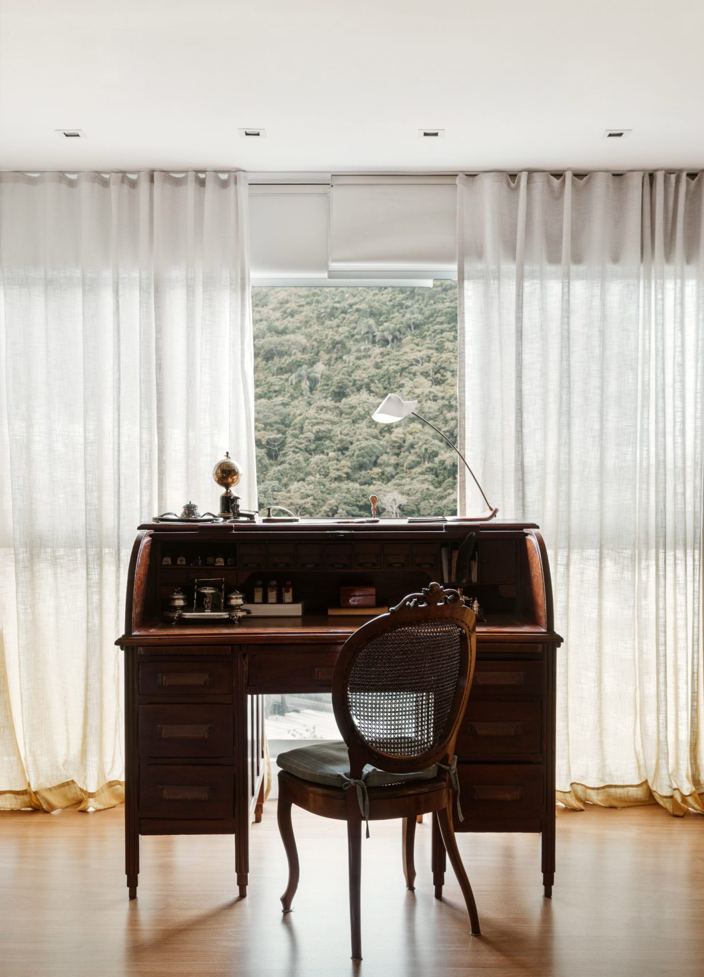 na foto escrivaninha e cadeira de madeira e cortina na janela