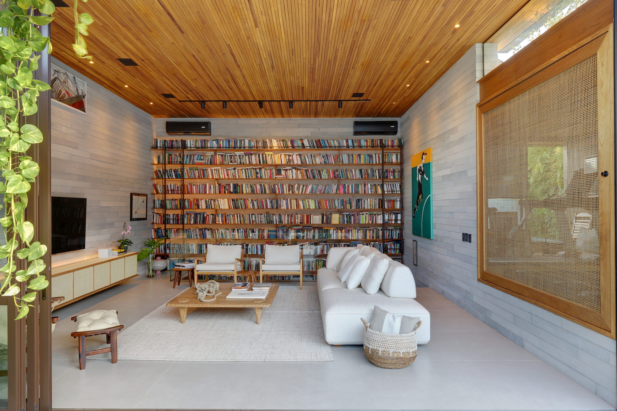 na foto grande sala com sofá, poltrona, mesinha de centro e grande estante com livros