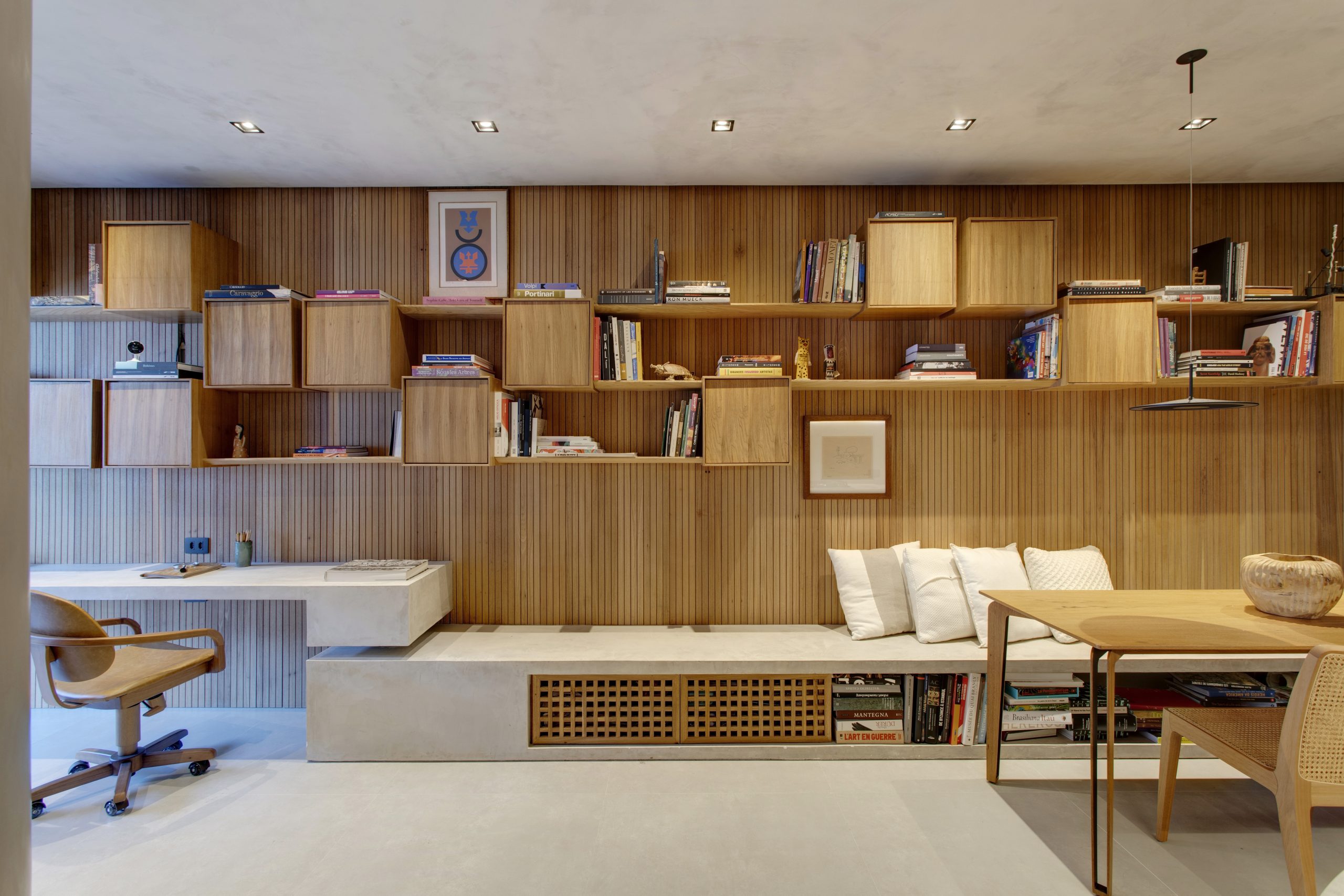 na foto cozinha e escritório integrados numa arquitetura fluida. a madeira predomina nas paredes e móveis,.